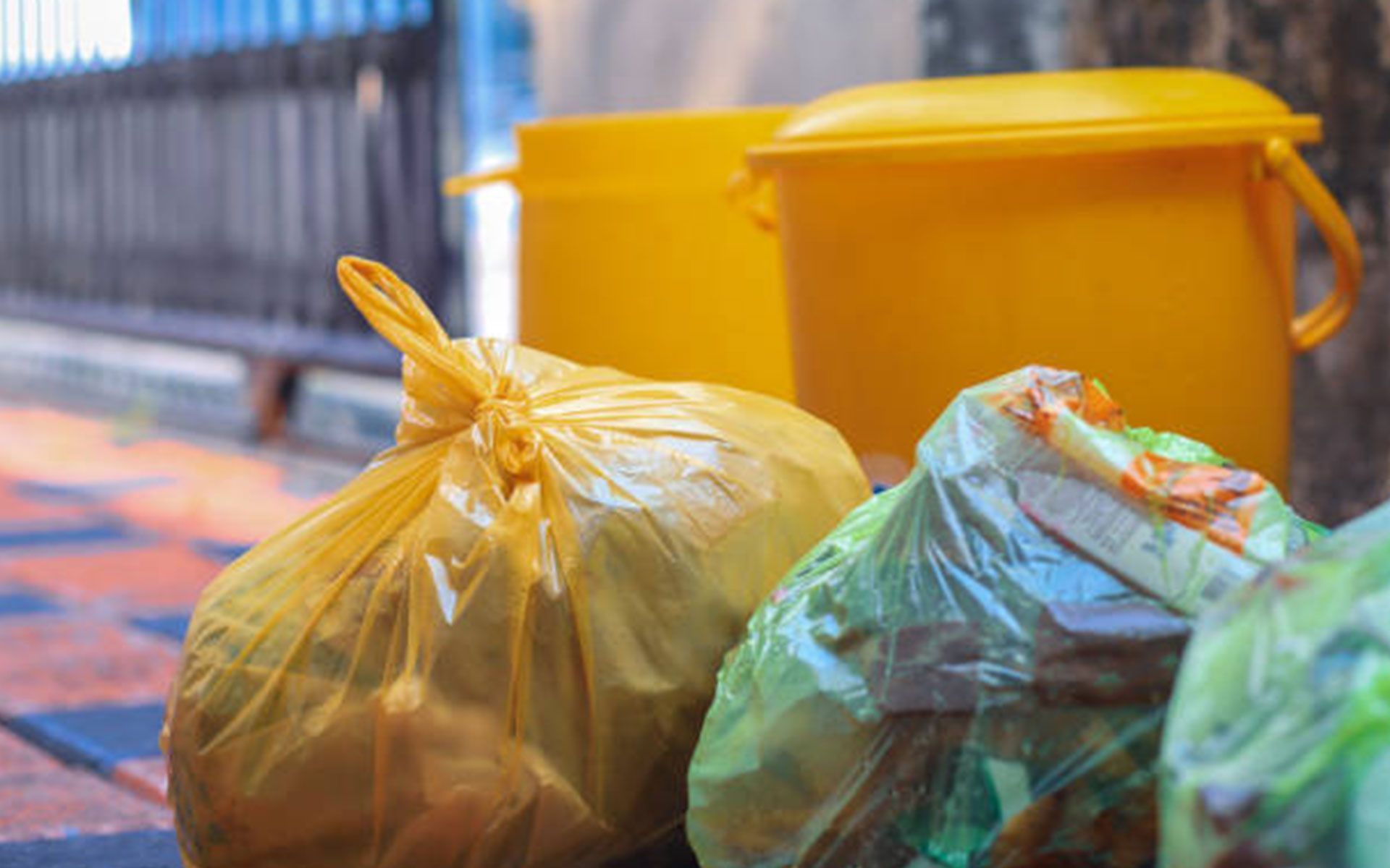 A bunch of trash bags are sitting on the ground next to a yellow trash can.