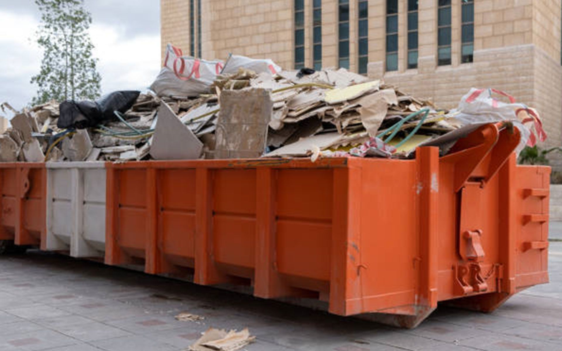 A large orange dumpster filled with trash is parked in front of a building.