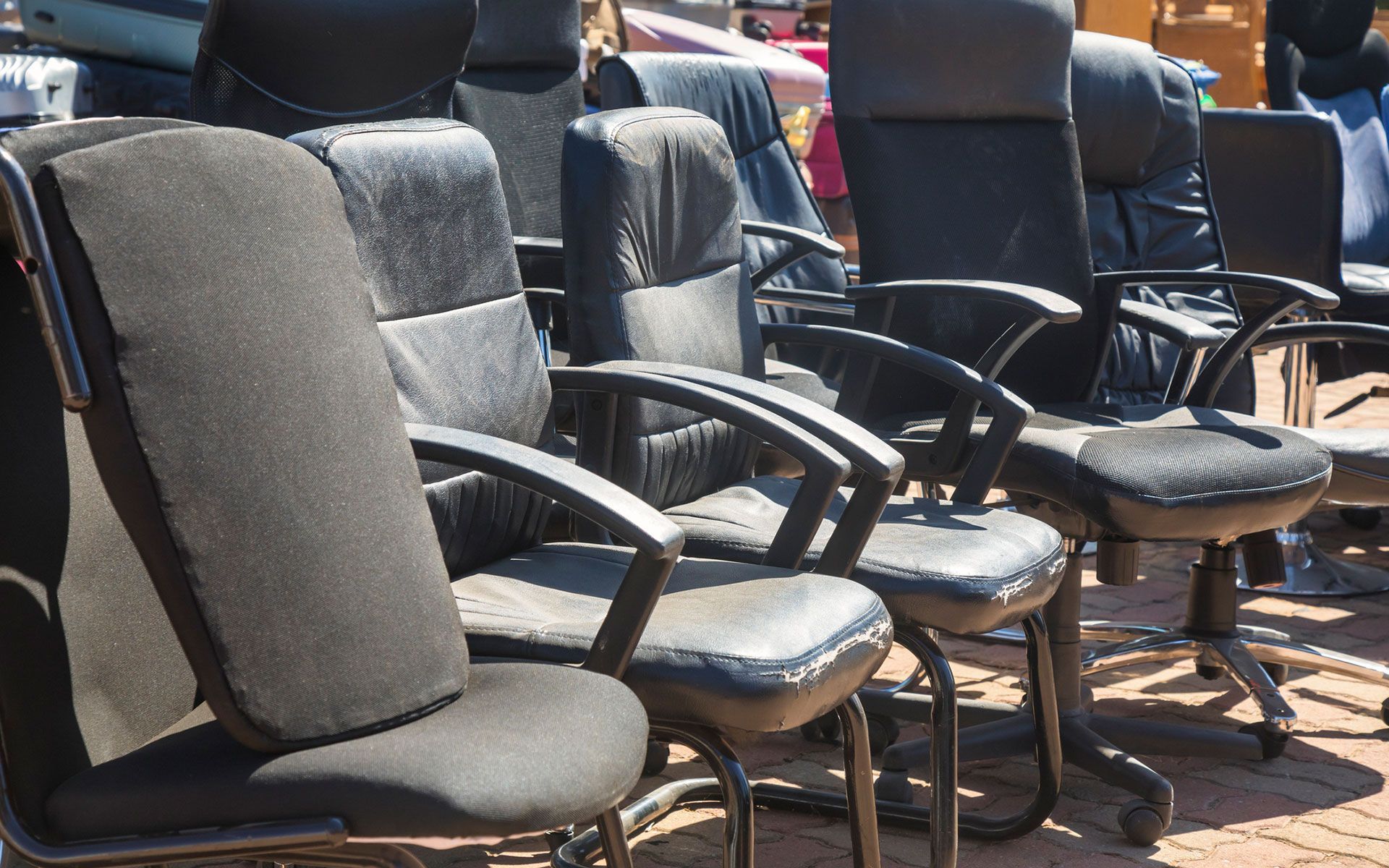 A row of black office chairs are lined up on a brick sidewalk.