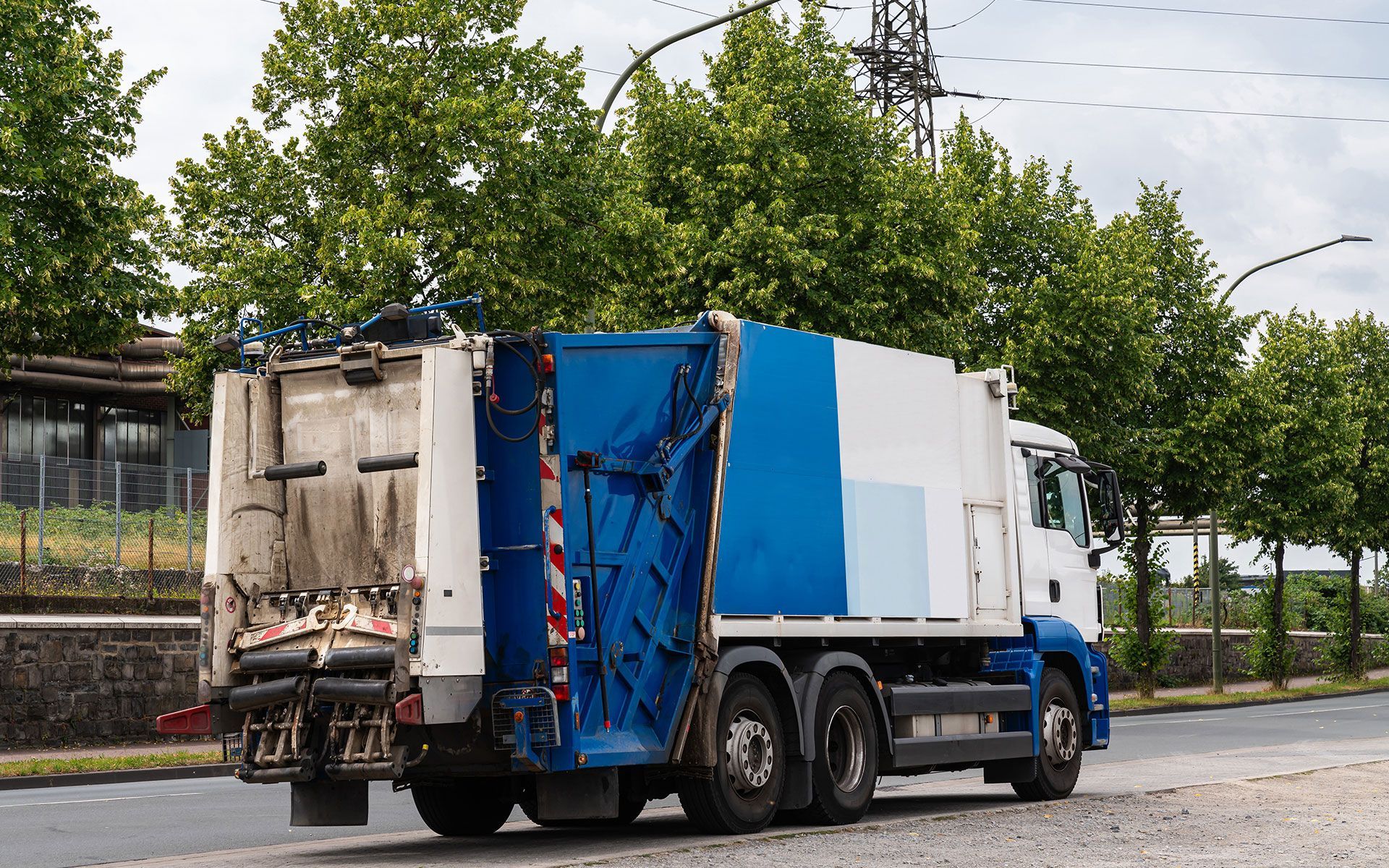 A blue and white garbage truck is driving down a street.