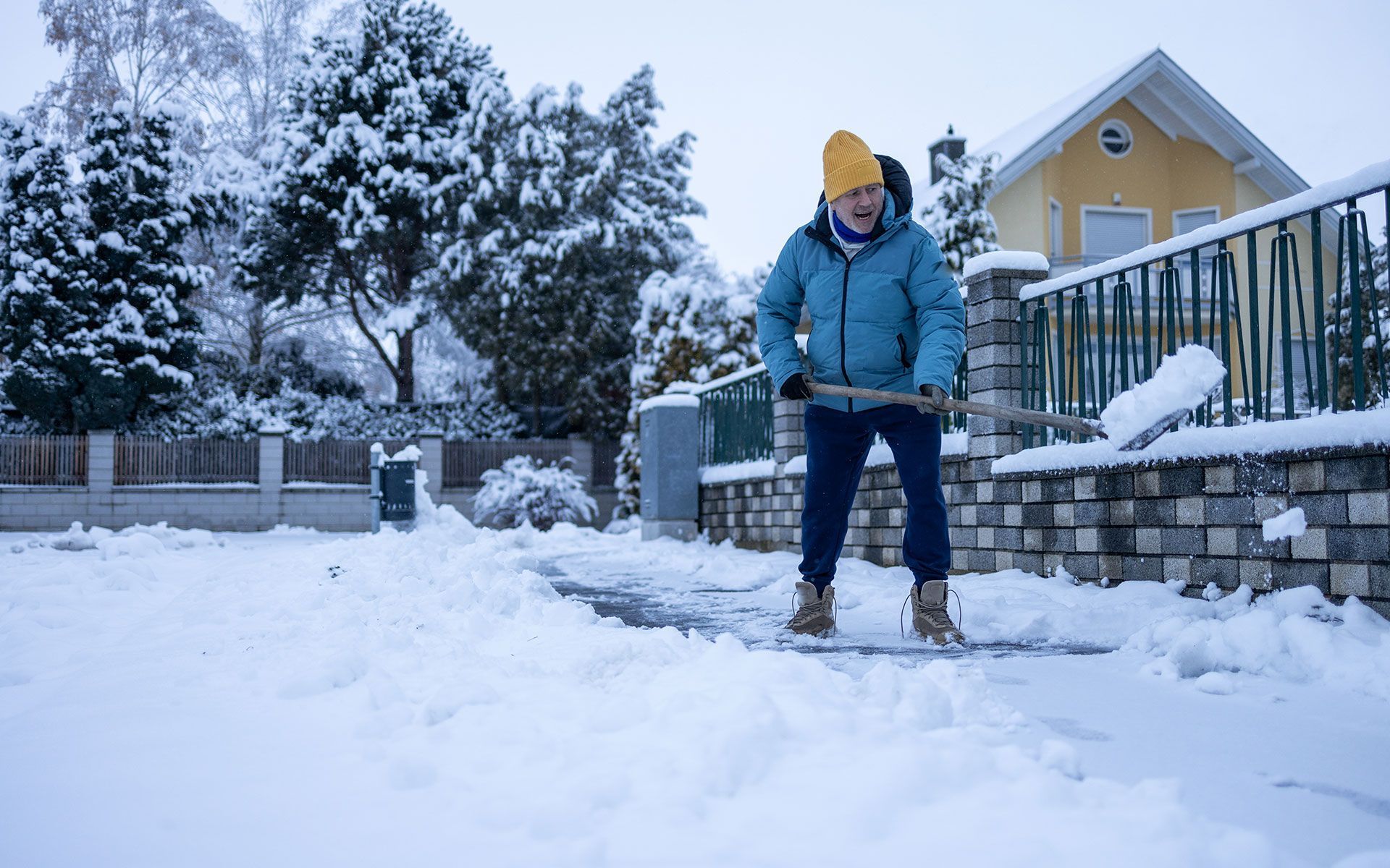 A man is shoveling snow from the sidewalk in front of a house.