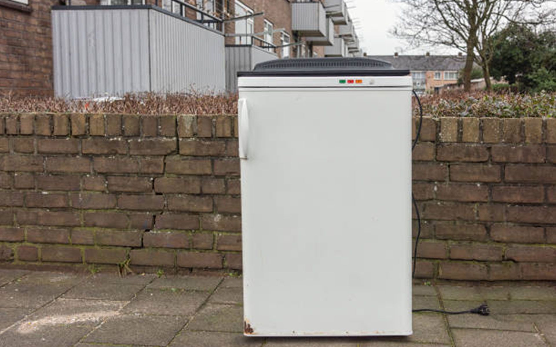A white refrigerator is sitting in front of a brick wall.