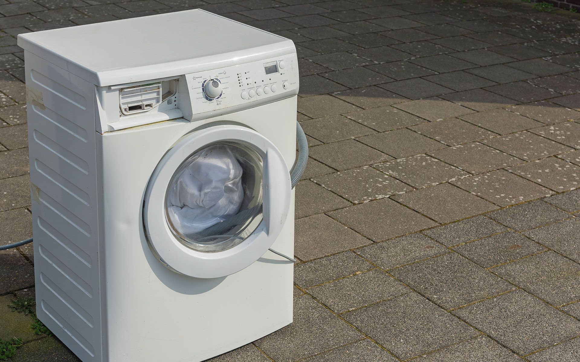 A white washing machine is sitting on a brick sidewalk.