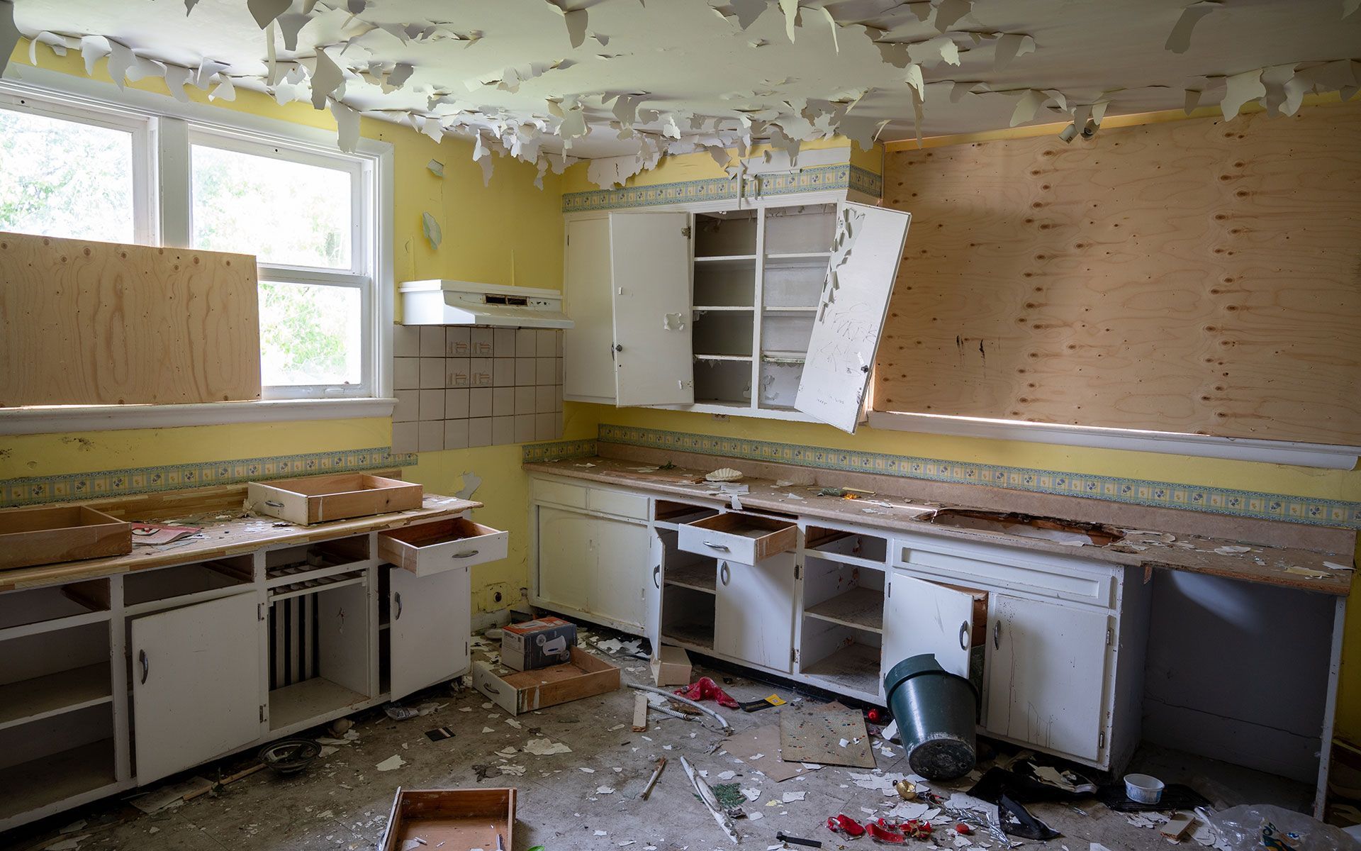 An abandoned kitchen with broken cabinets and a bucket on the floor.