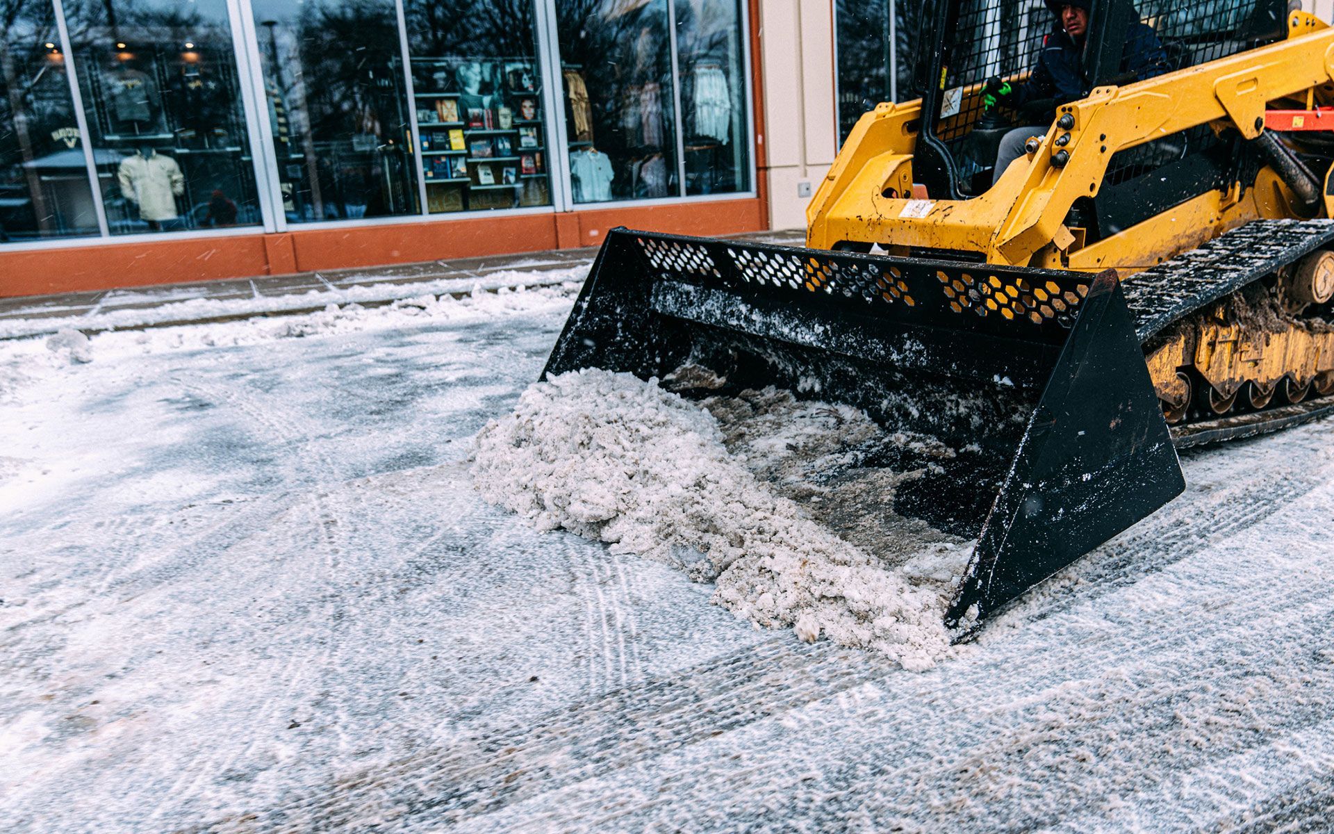 A bulldozer is clearing snow from the sidewalk in front of a building.