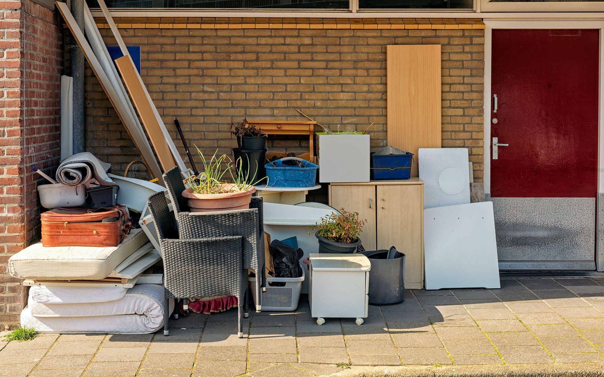 A pile of junk is sitting on the sidewalk in front of a brick building.
