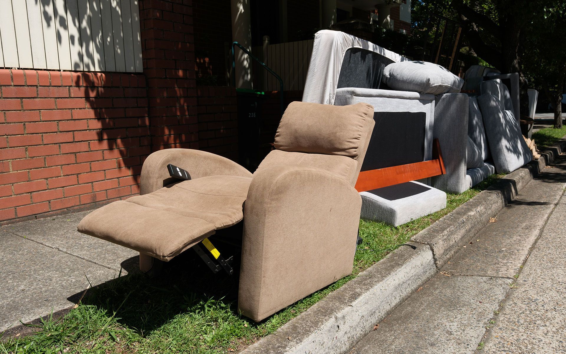 A recliner is sitting on the side of the road next to a pile of furniture.