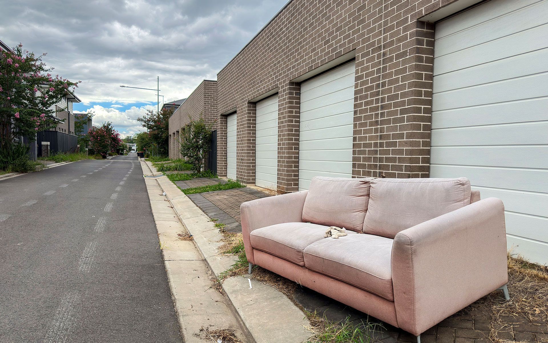 A pink couch is sitting on the side of the road next to a garage door.
