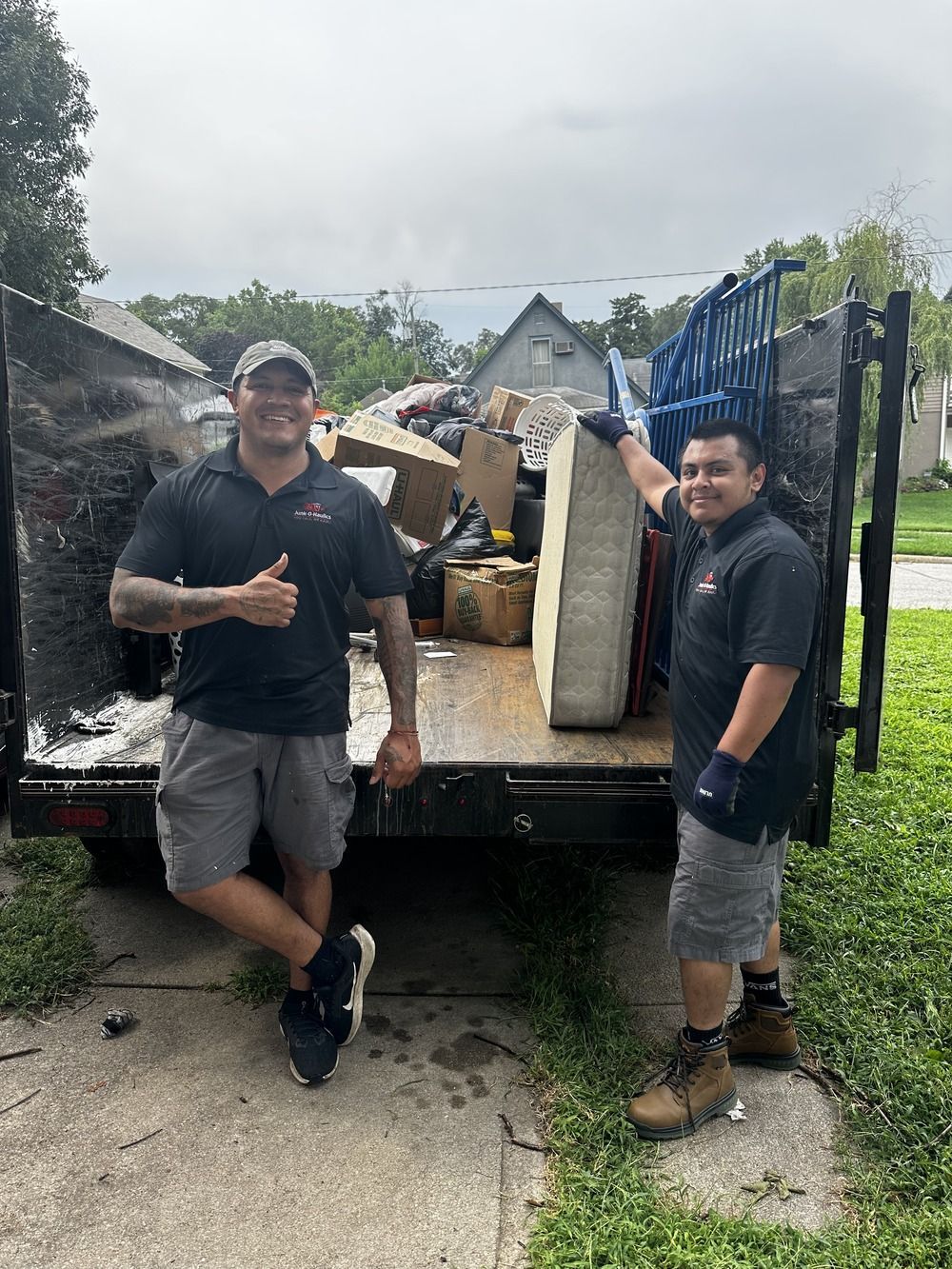 A man in an orange vest is carrying a green trash can.