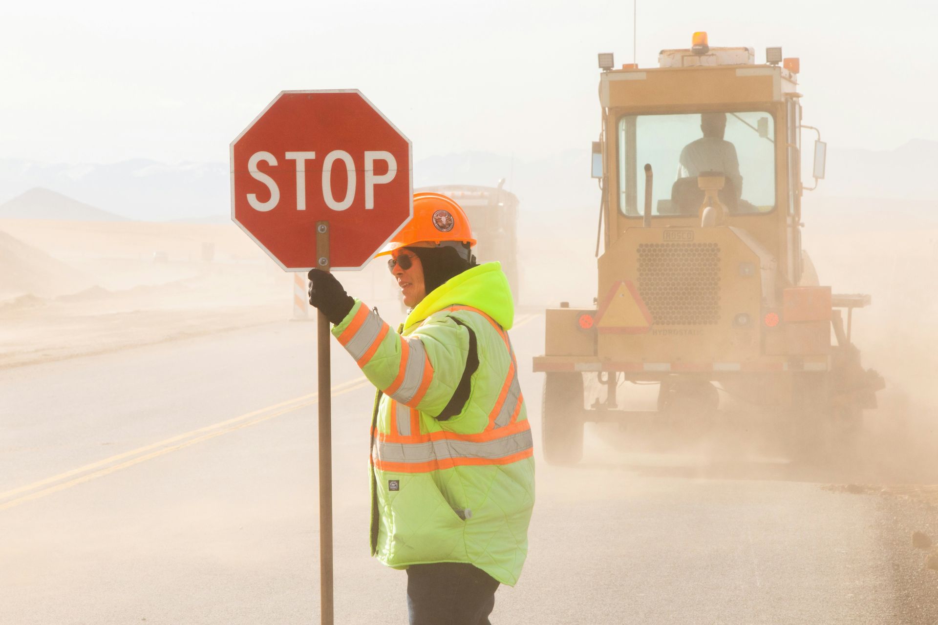 A woman is holding a stop sign in front of a bulldozer.