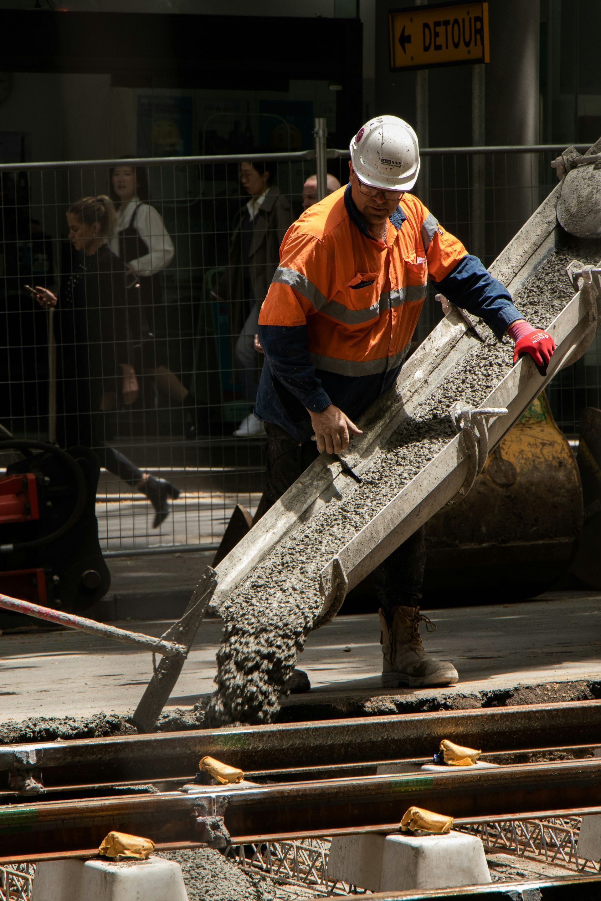 A man wearing a hard hat is pouring concrete on a sidewalk.