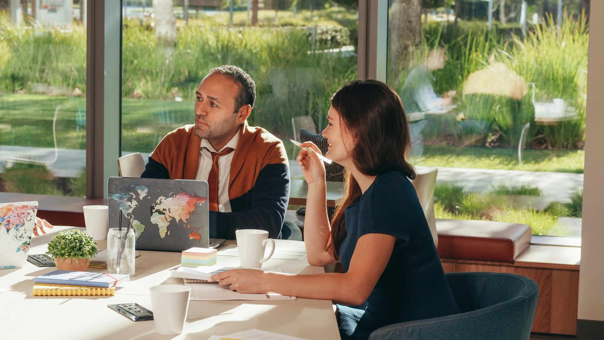 A man and a woman are sitting at a table with laptops.