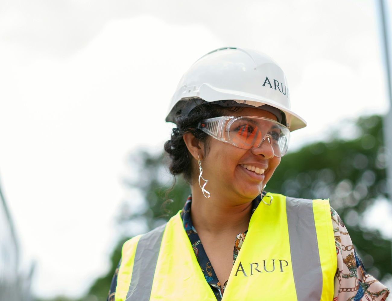 A woman wearing a hard hat and safety vest is smiling.