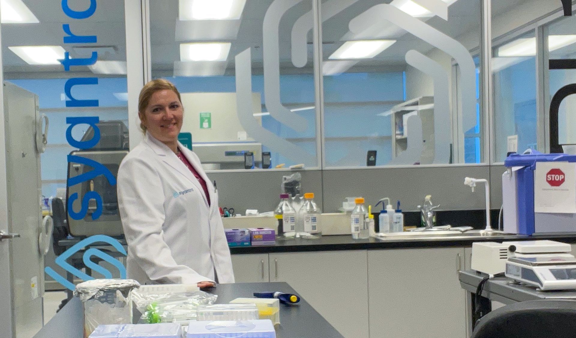 Olesya Kharenko stands in front of Syantra lab in lab coat.