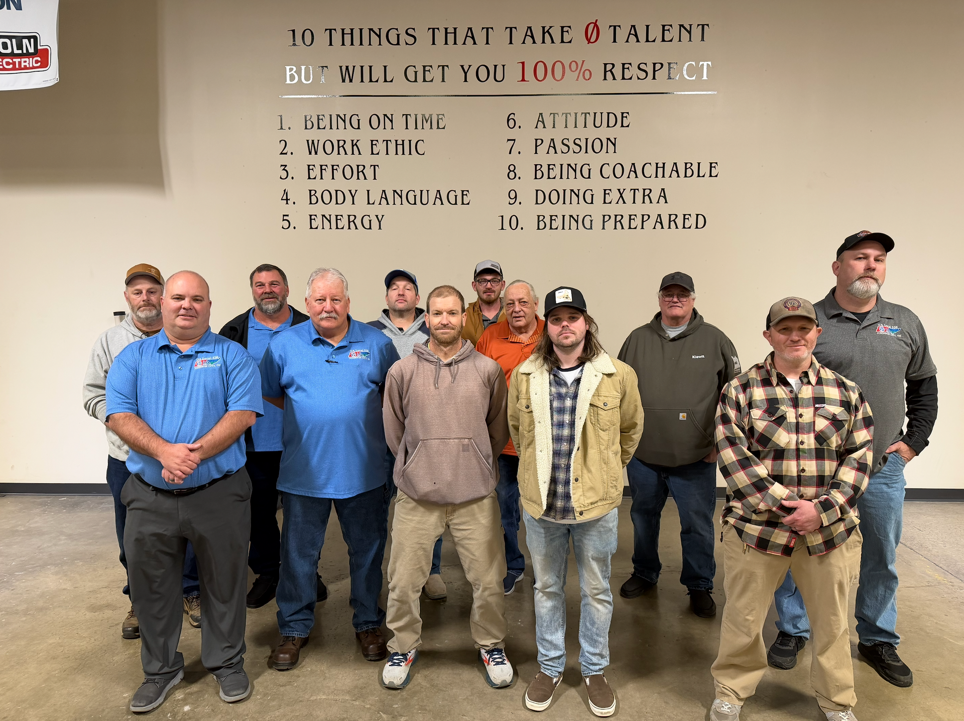 Group of men posing in front of a wall with text about respect; inside building.