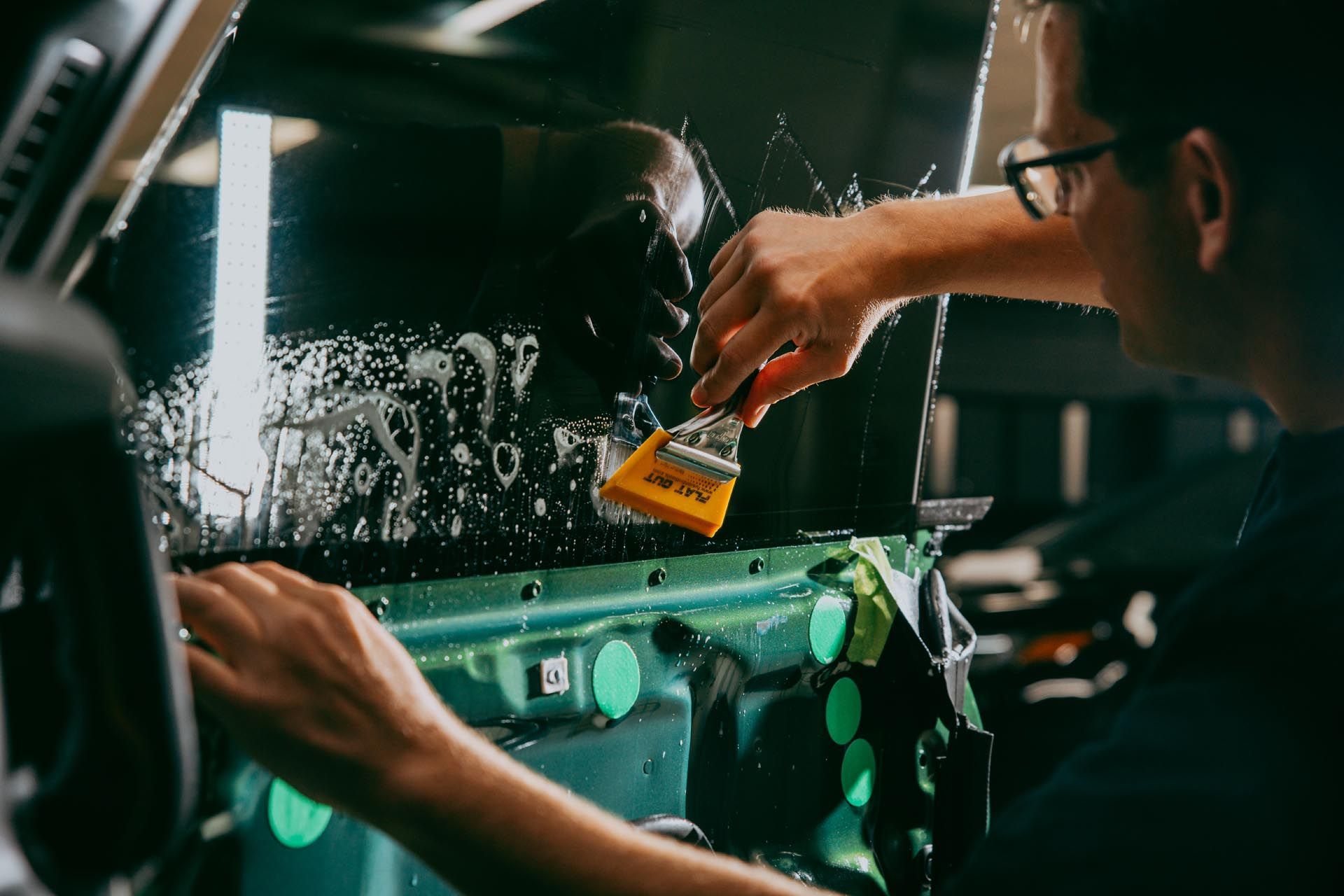 A man is cleaning a car window with a brush.