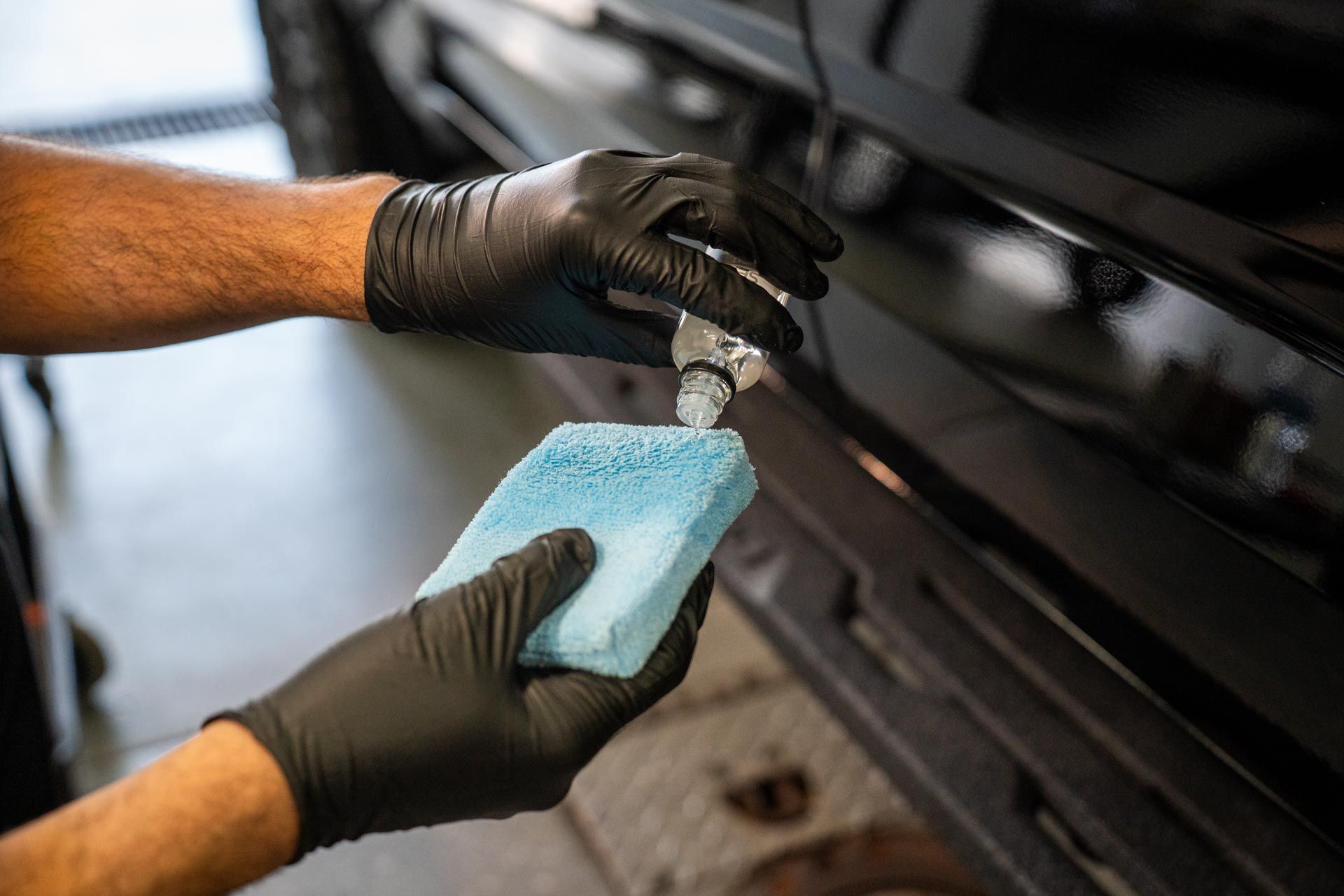 A man wearing black gloves is cleaning a car with a sponge.