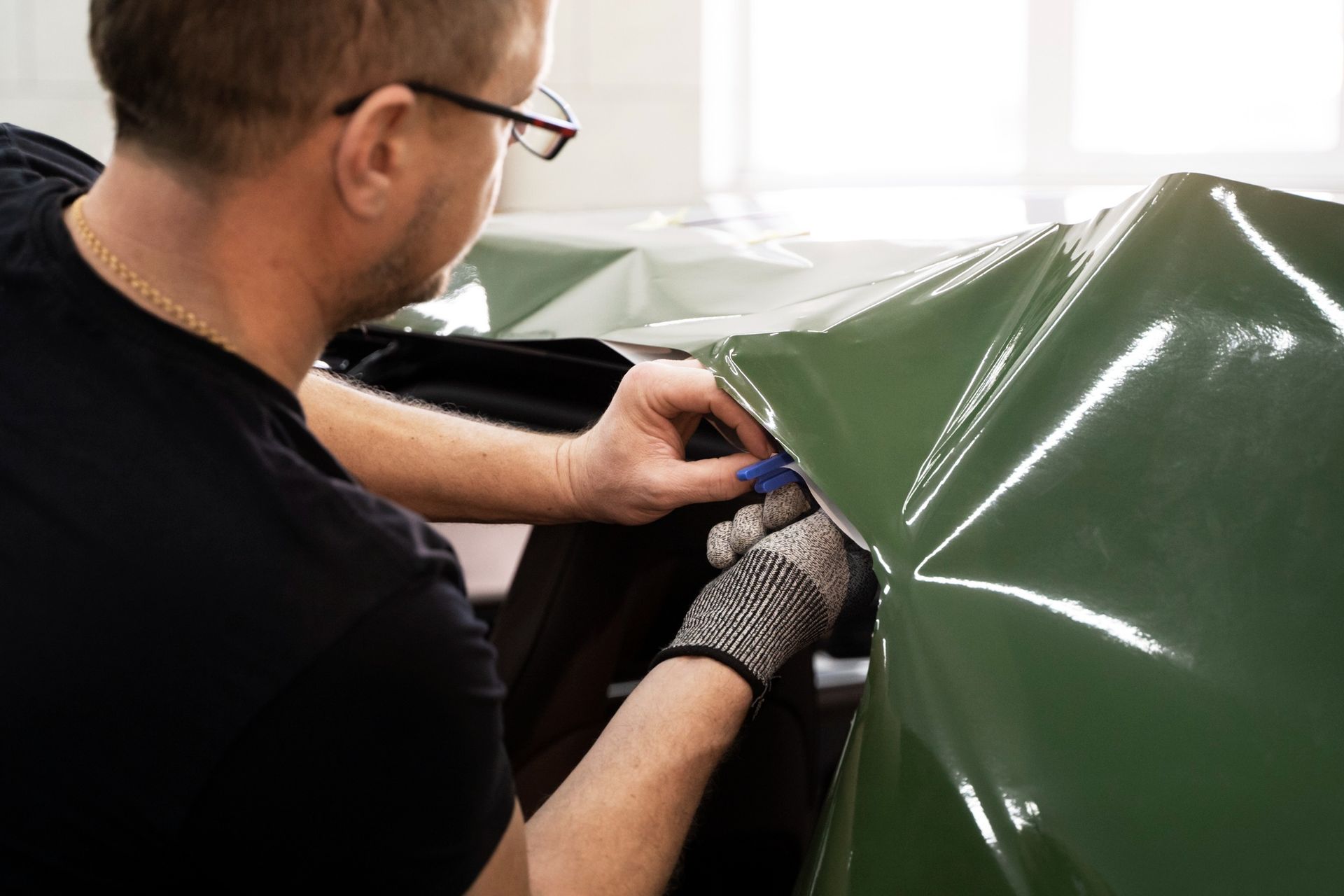 A man is wrapping a car in green vinyl.