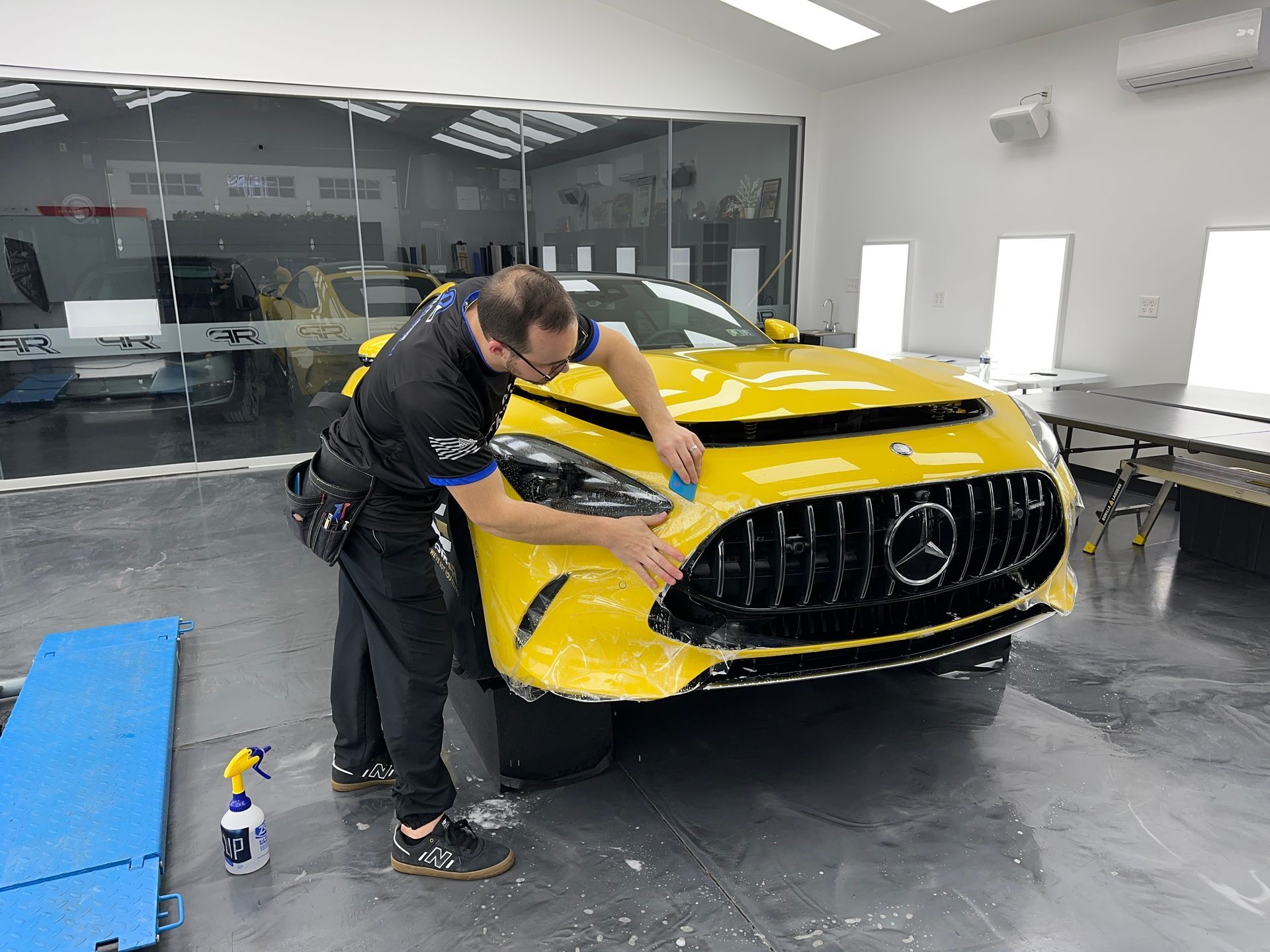 A man is applying a protective film to the headlights of a mercedes benz.