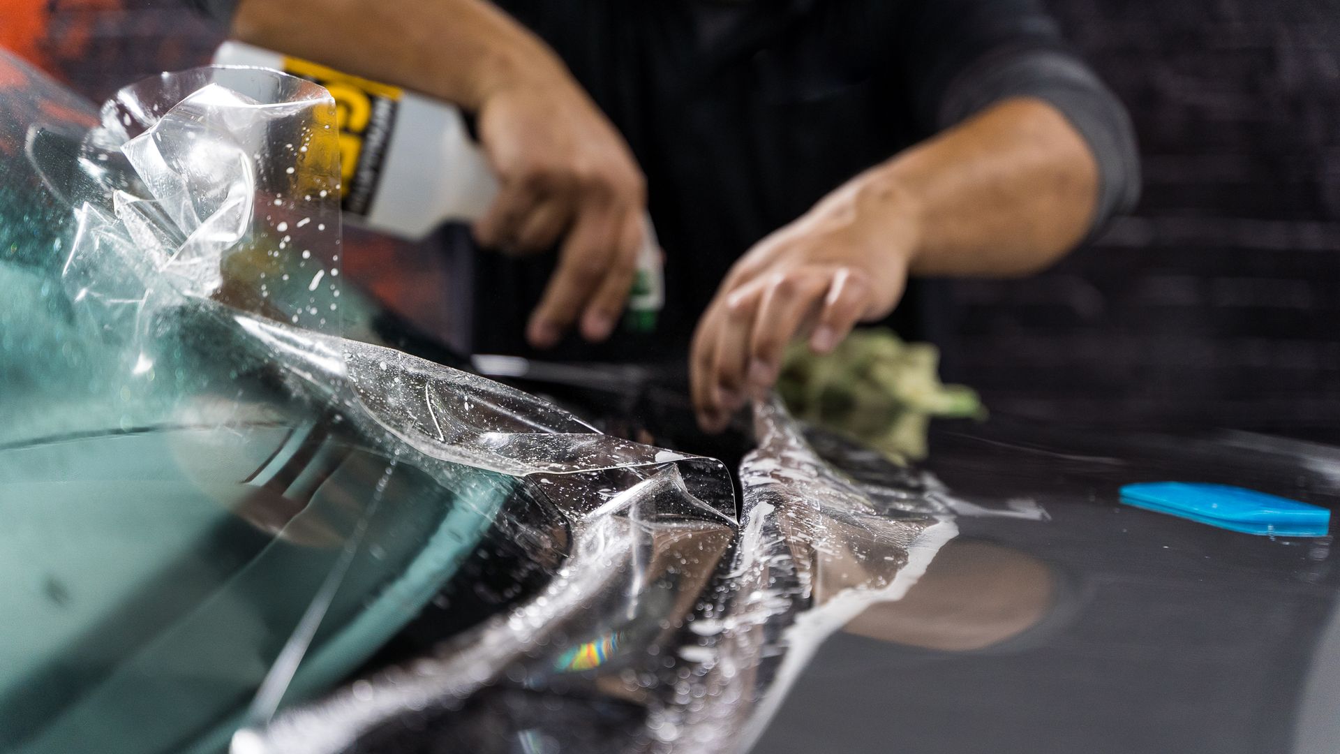 A man is applying a clear plastic film to the windshield of a car.