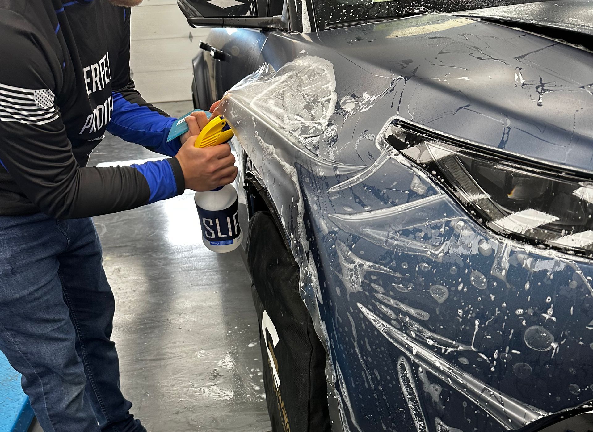 A person is applying protective film to a blue car.