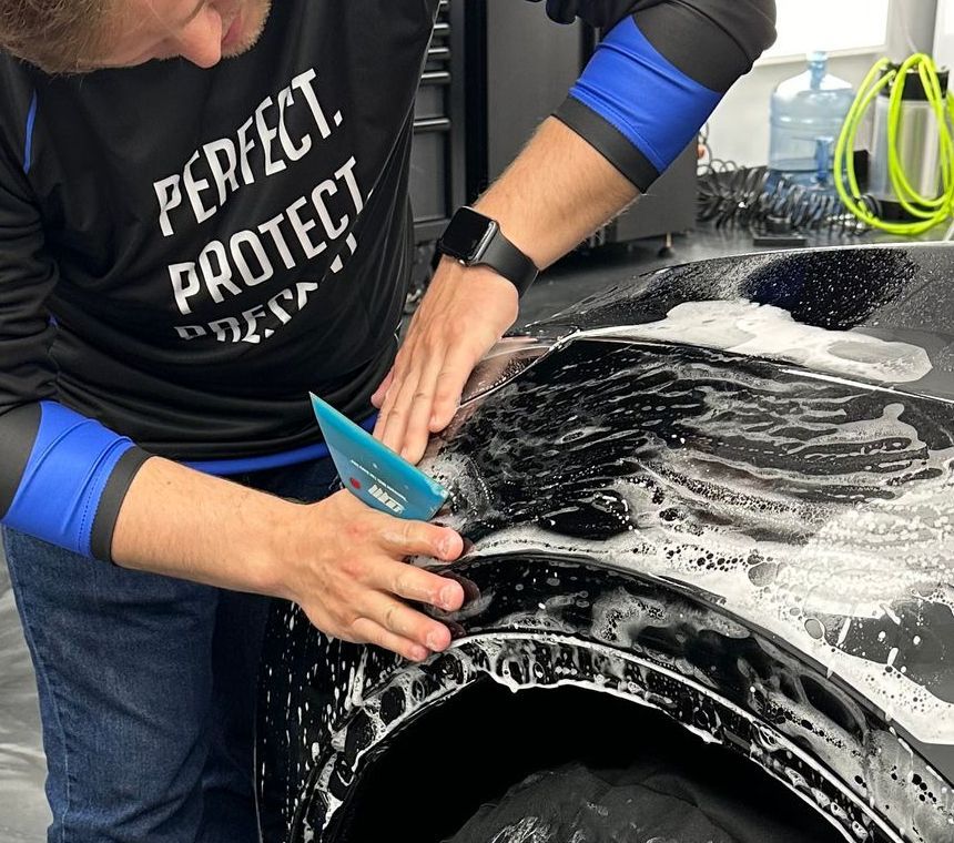 A woman is applying a protective film to the side of a car.
