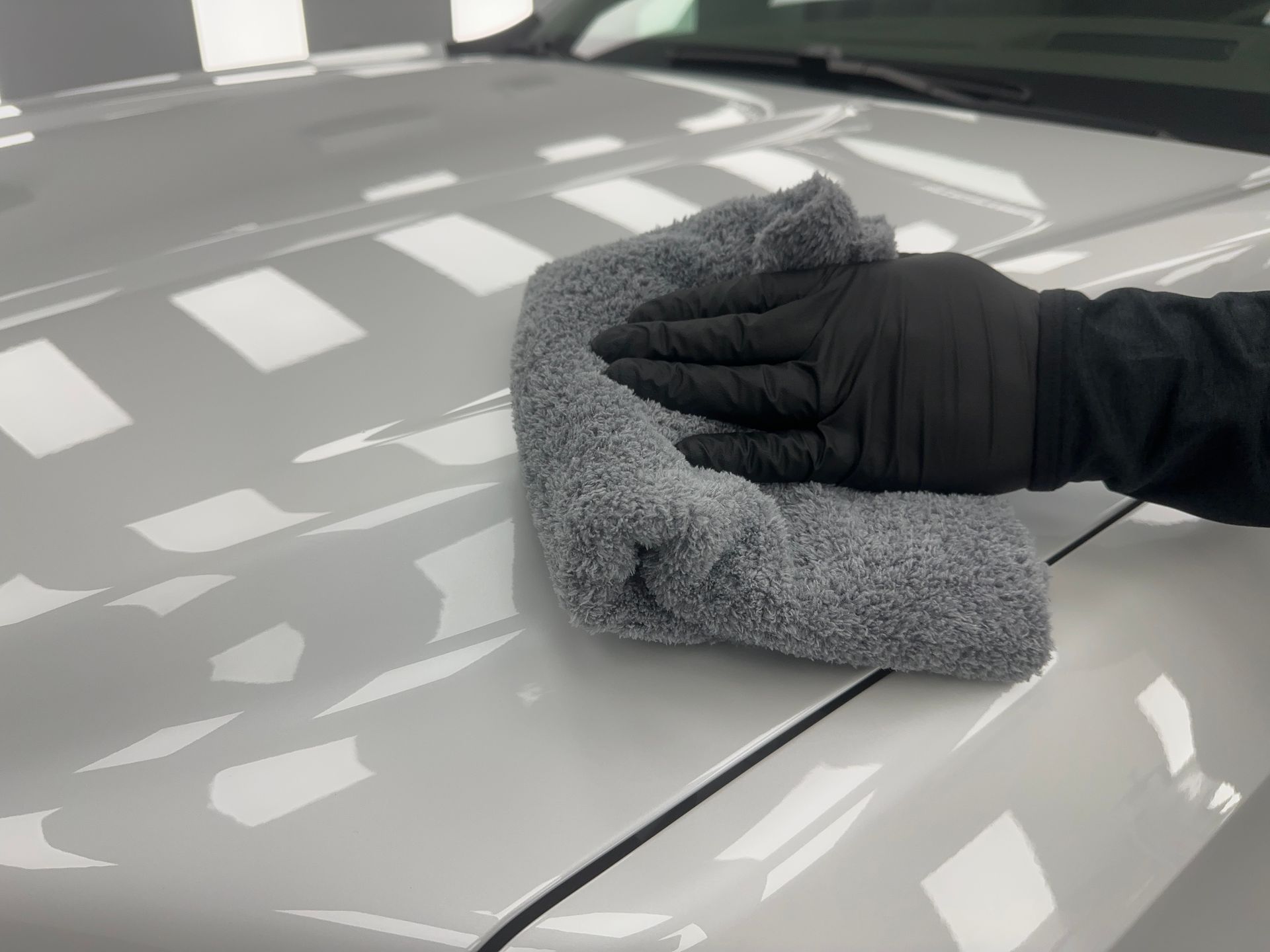 A person is cleaning a black car with a yellow cloth.