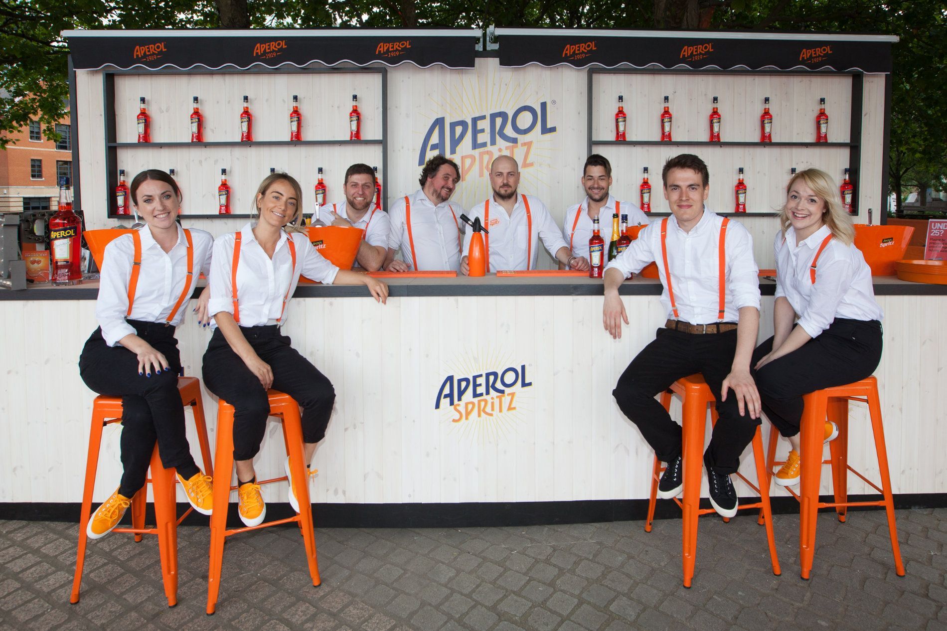 a group of people sitting on stools in front of an aperol bar