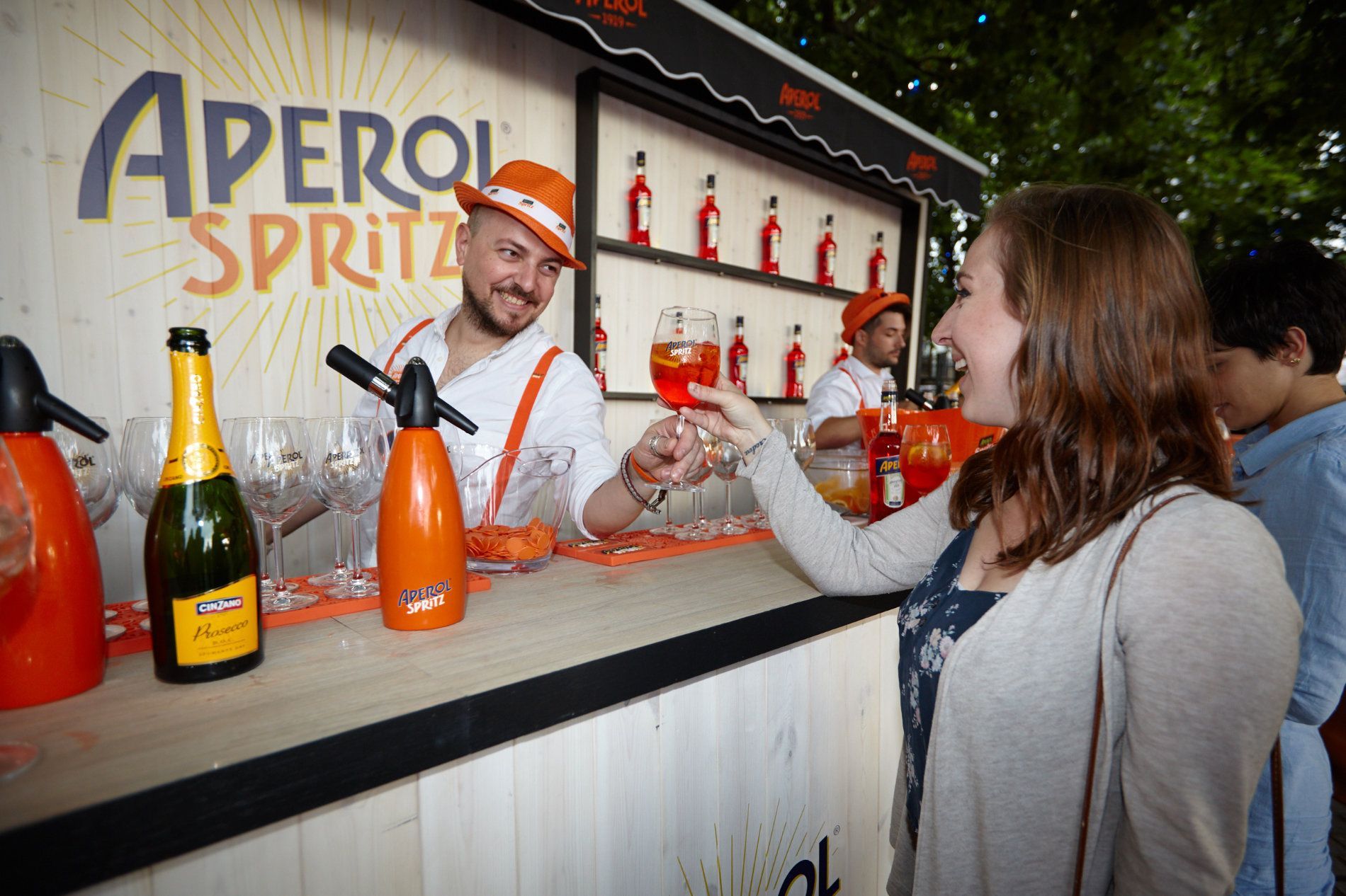 a woman is standing in front of an aperol spritz bar .