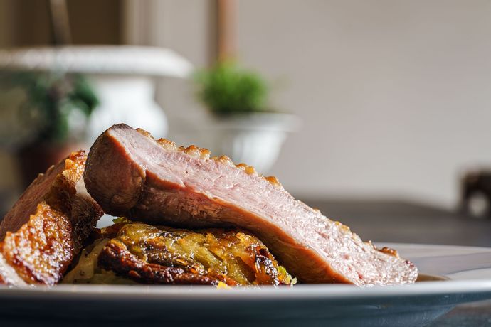 Slices of glazed meat stacked on a plate, with a blurred kitchen background