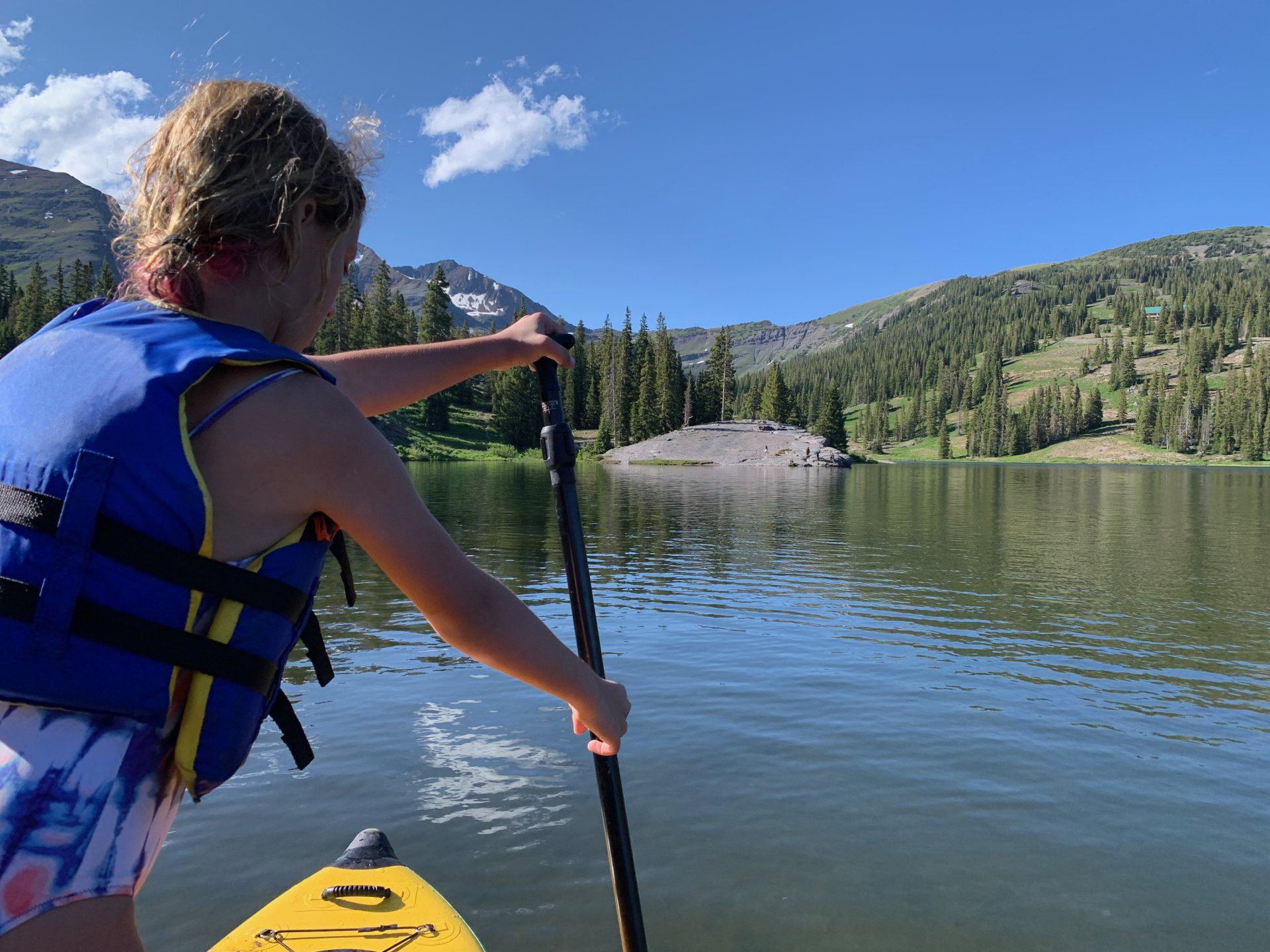 A young girl is paddling a yellow kayak on a lake.