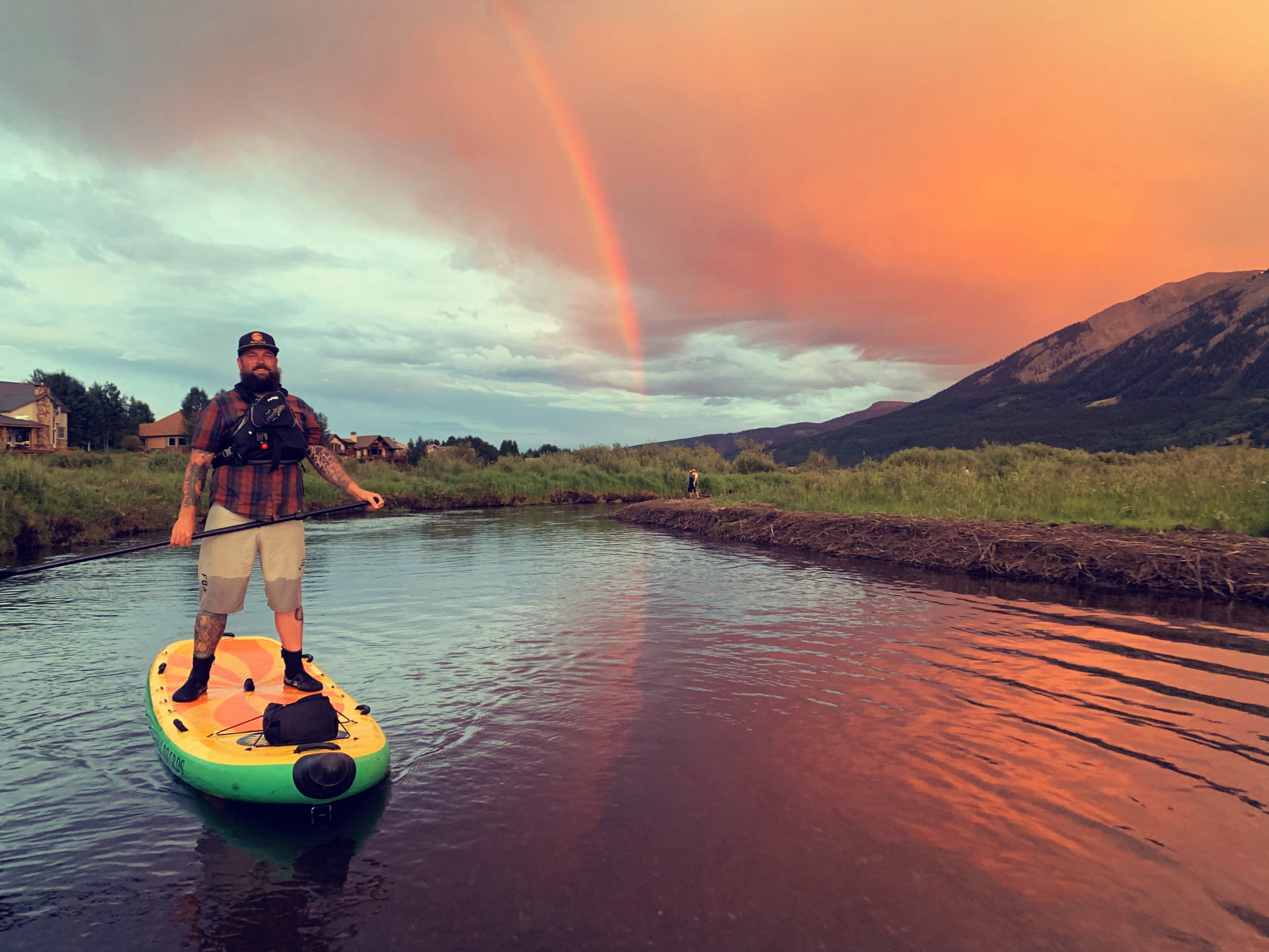 man paddleboarding on lake with rainbow in background