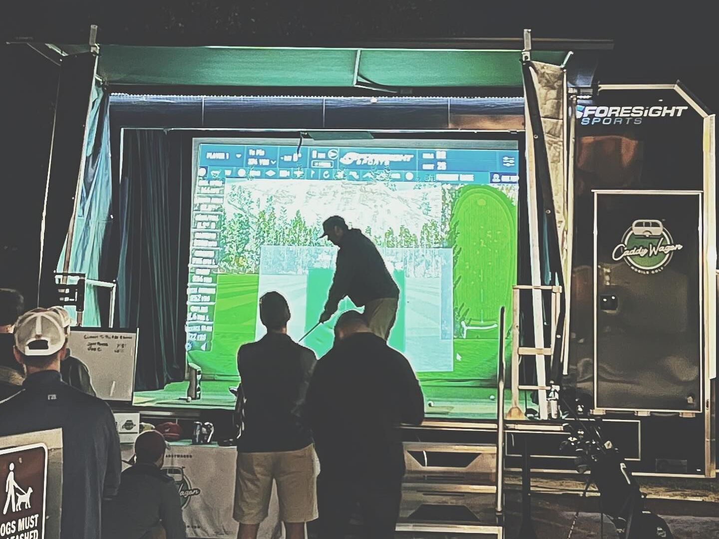 A group of people are standing in front of a golf simulator.