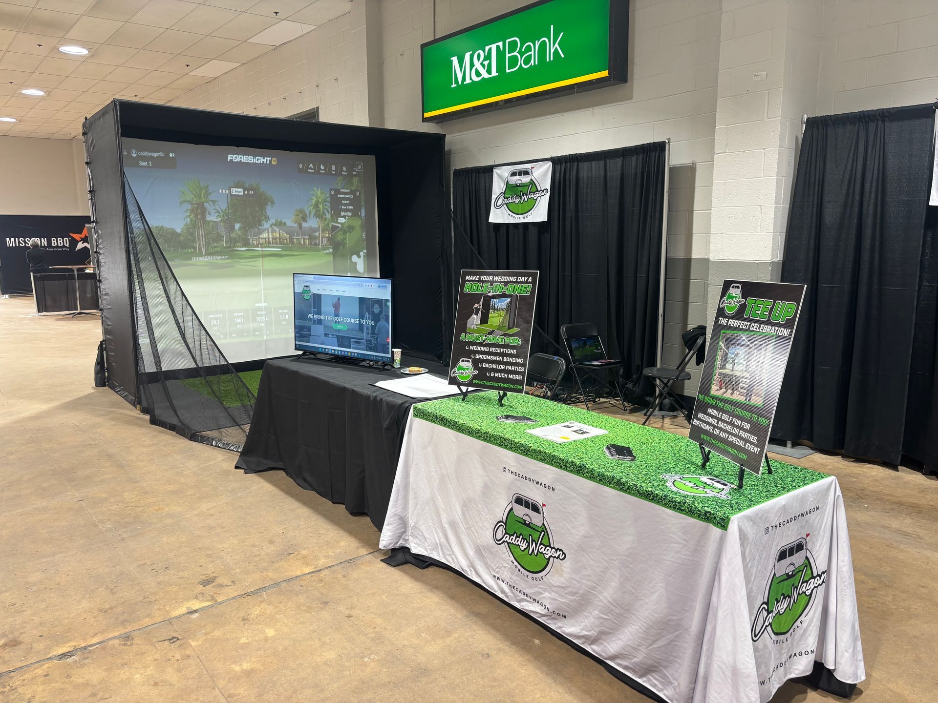 A golf simulator is sitting in a room next to a table.