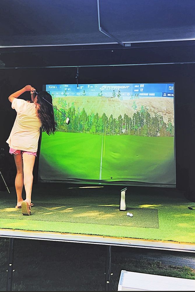 A woman is playing golf in front of a large screen.