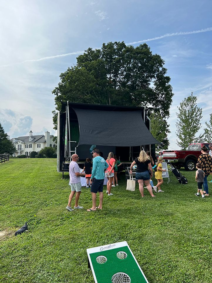A group of people are standing in a grassy field in front of a trailer.