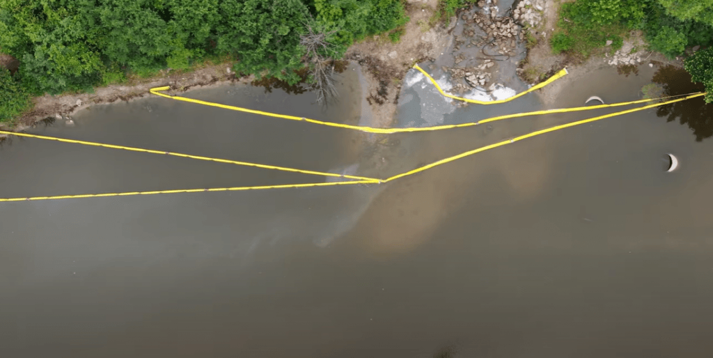 Booms collect chemicals spilled into the Flint River, but sheen can be seen passing through