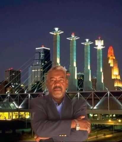 Man with crossed arms in front of Kansas City skyline at night. Illuminated buildings and bridge.