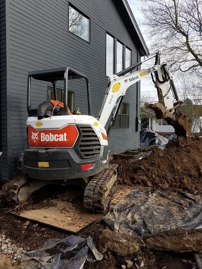 A bobcat excavator is digging a hole in front of a house.