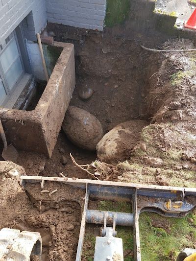 A large rock is laying in the dirt in front of a house.