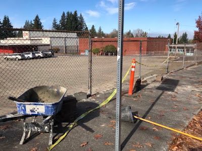 A wheelbarrow is sitting in a parking lot next to a chain link fence.