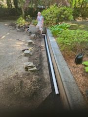 A man is standing next to a drain pipe in a yard.