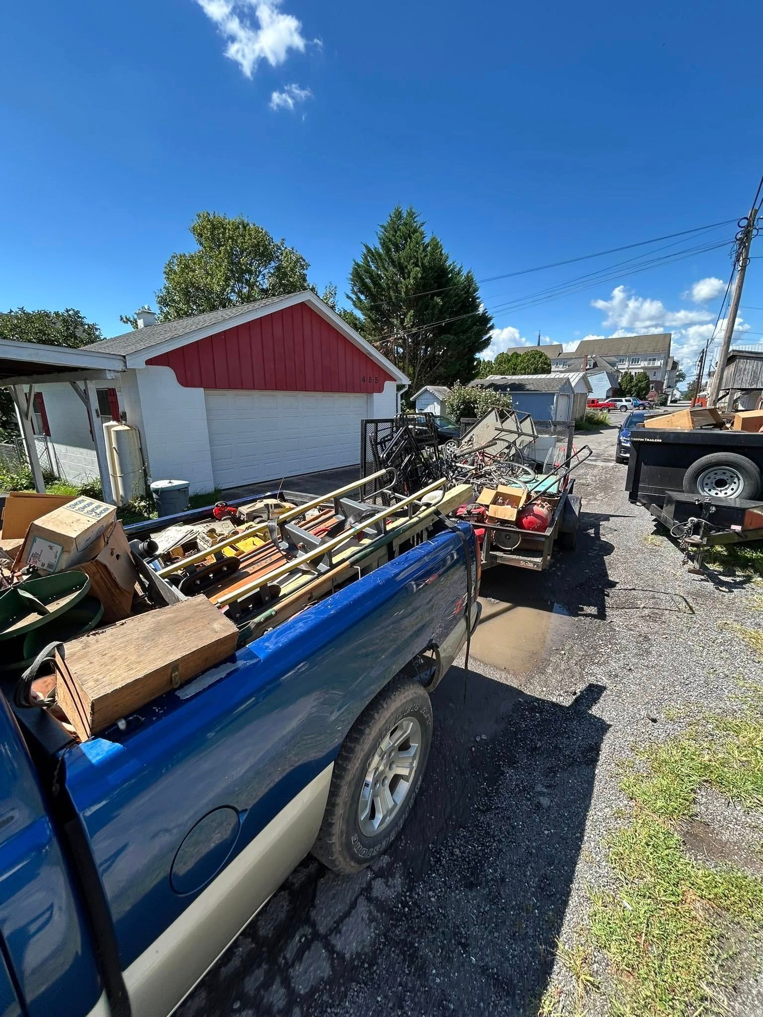 Blue pickup truck loaded with items, parked next to a building with red trim. Outdoor shot, bright sky.