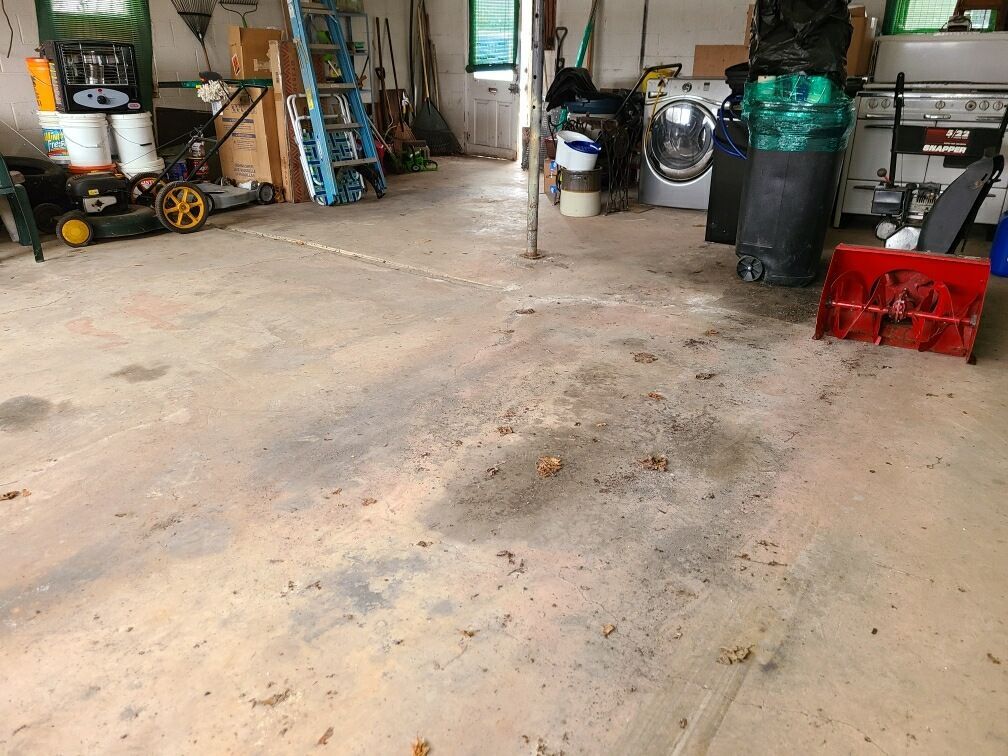 A cluttered garage with a concrete floor, featuring tools, a snowblower, and a washing machine.