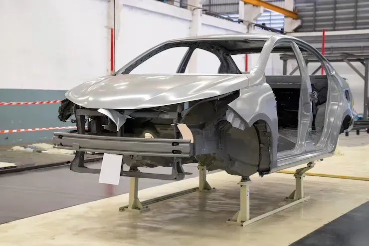 Two mechanics in work uniforms discuss repairs while standing before an open car hood in a garage.