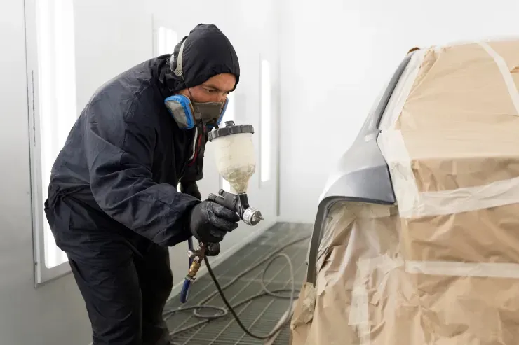 A mechanic works on a car engine while using a red refrigerant service machine in an auto shop.