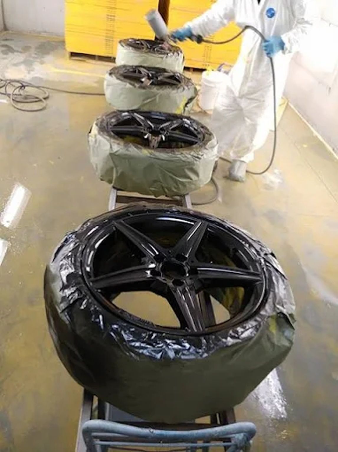 A technician in blue overalls kneels to inspect the vent on the side of a parked camper van on a sunny day.