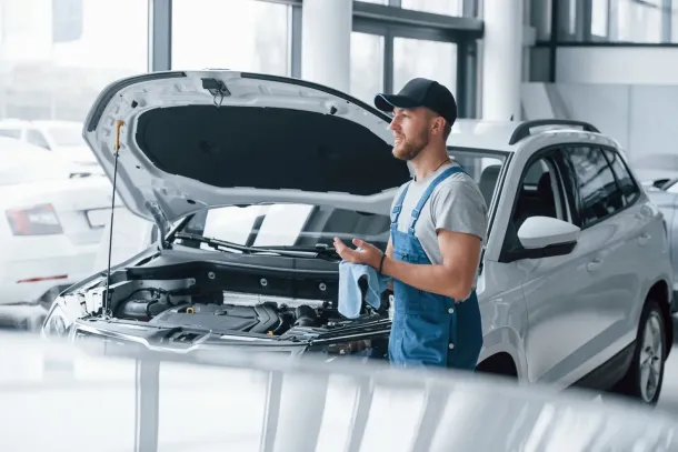 A mechanic wearing a blue uniform inspects a car’s brake system in a garage.