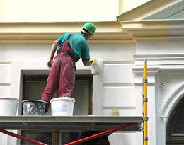 A man is painting the side of a building on a scaffolding.