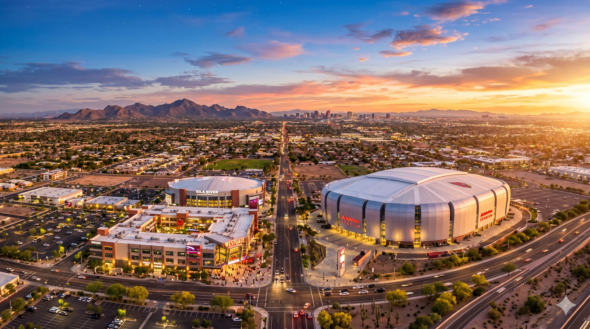 Aerial sunset view of a city with a large stadium, roads, mountains, and warm orange sky